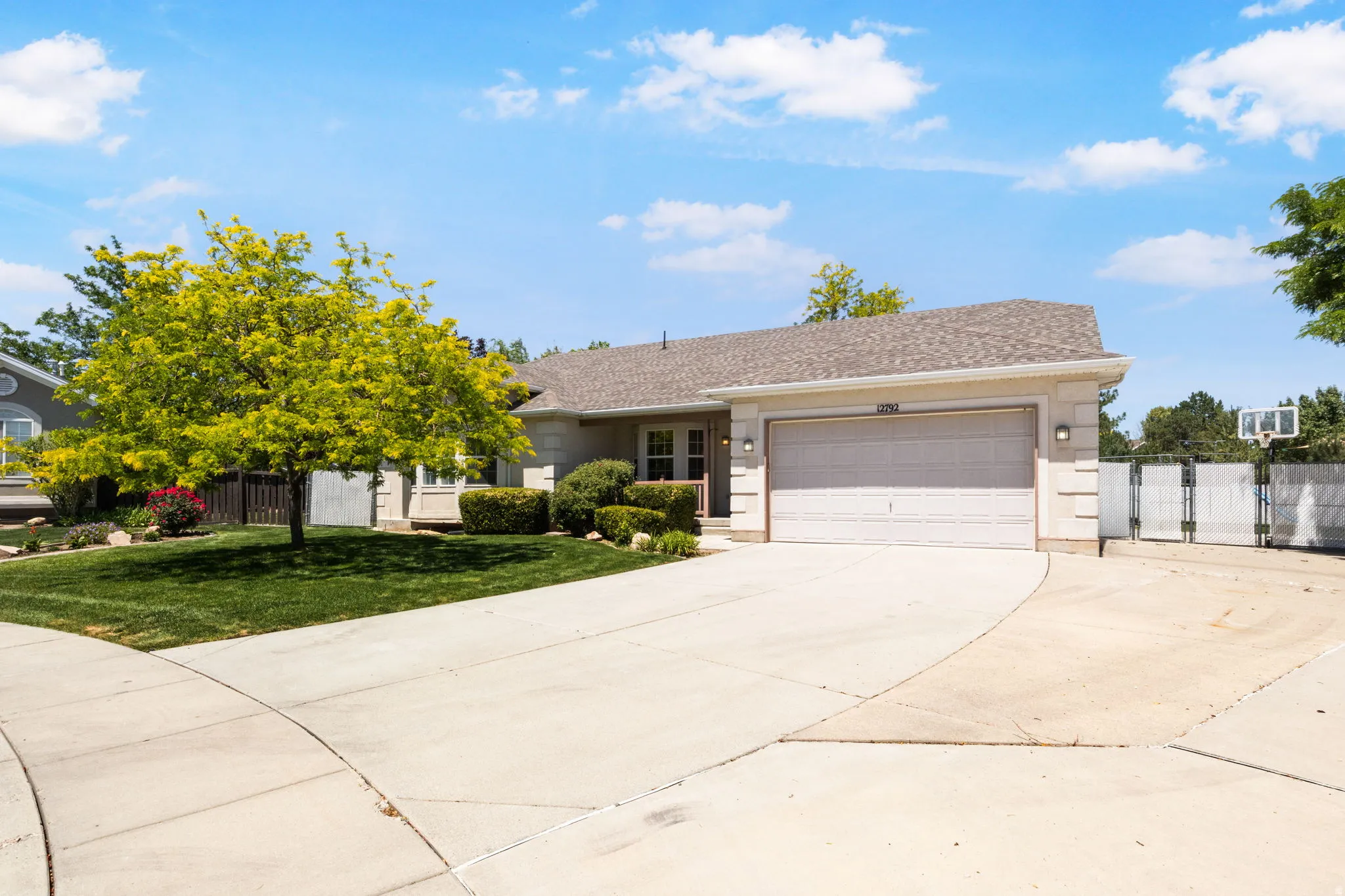 Ranch-style residence featuring a paved driveway, attached garage, and a manicured front lawn with mature trees and shrubs