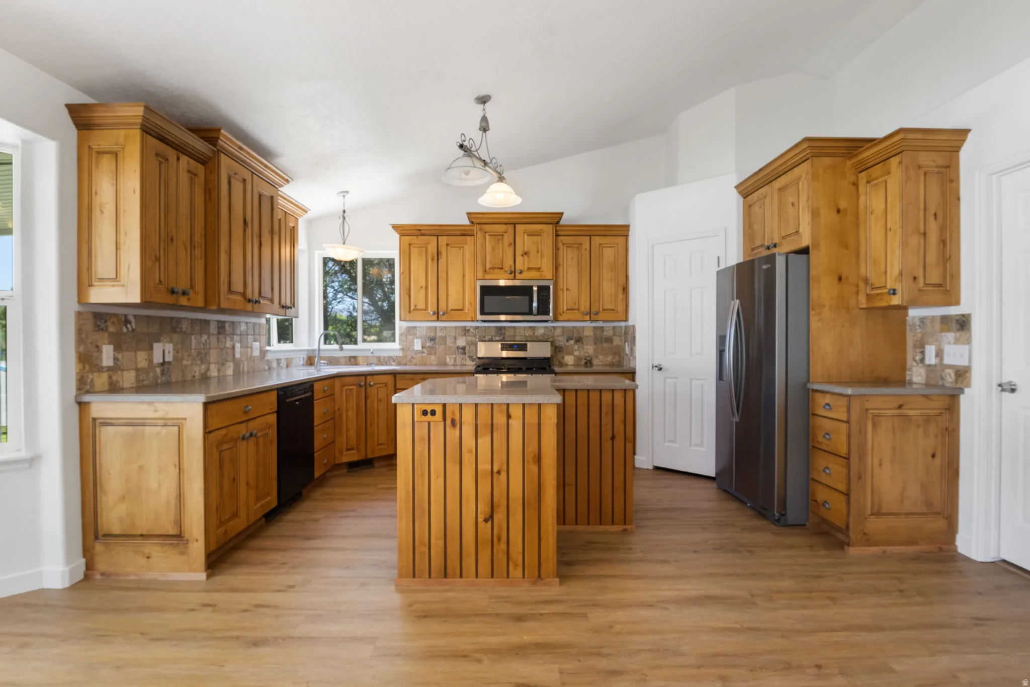 Spacious kitchen featuring extensive wood cabinetry, stone-finish countertops, and a full tile backsplash