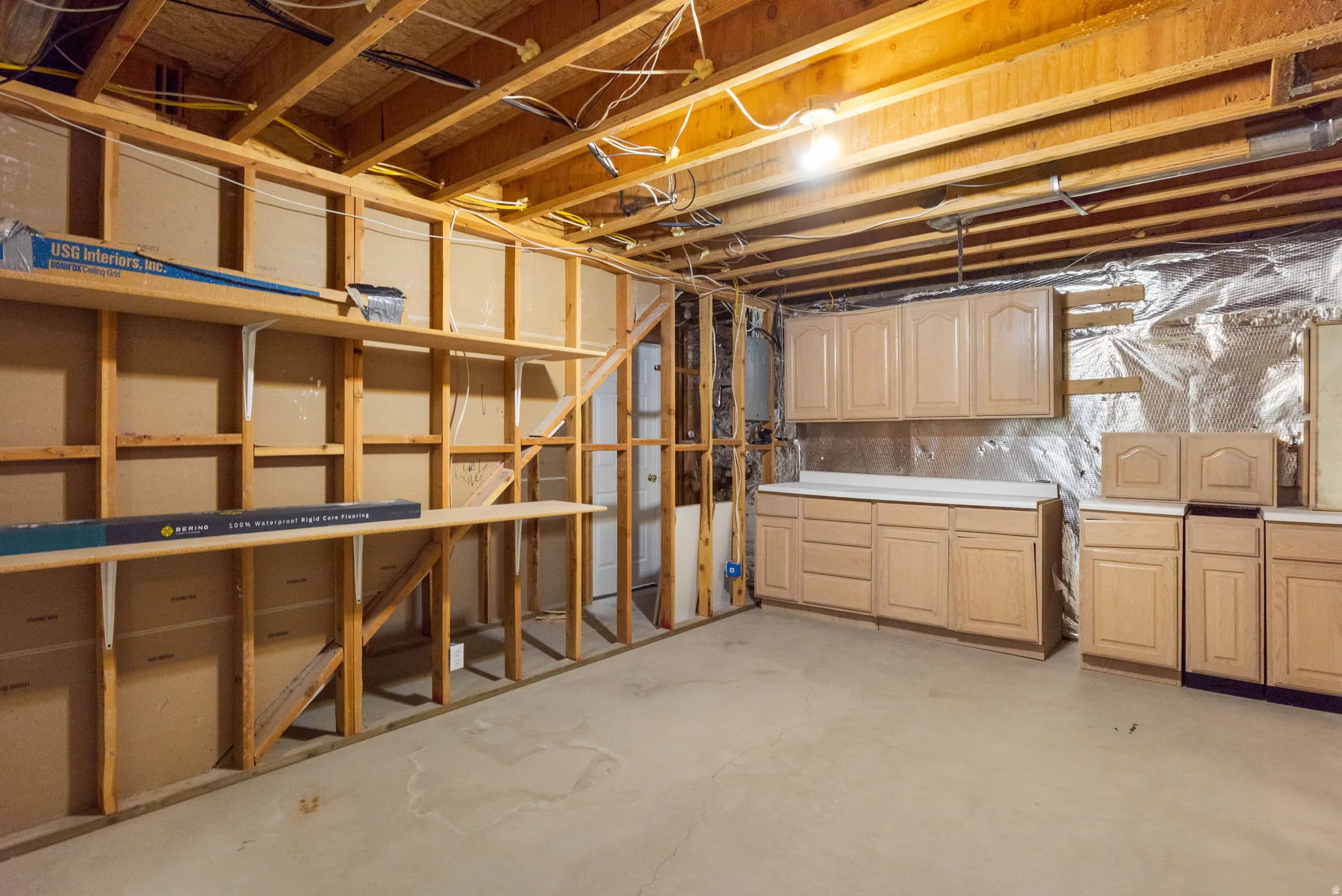 Unfinished basement with exposed wood framing, concrete flooring, built-in shelving, and installed cabinetry with countertops