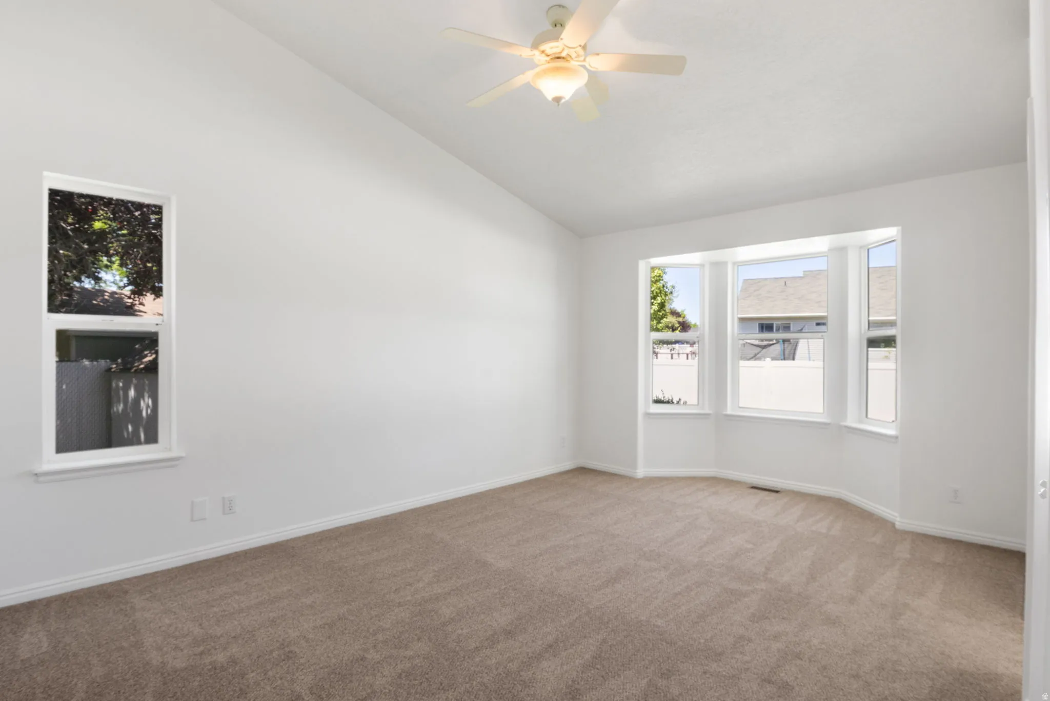 Spacious room featuring a bay window, a single vertical window, sloped ceilings, a ceiling fan with light fixture, and neutral carpet flooring