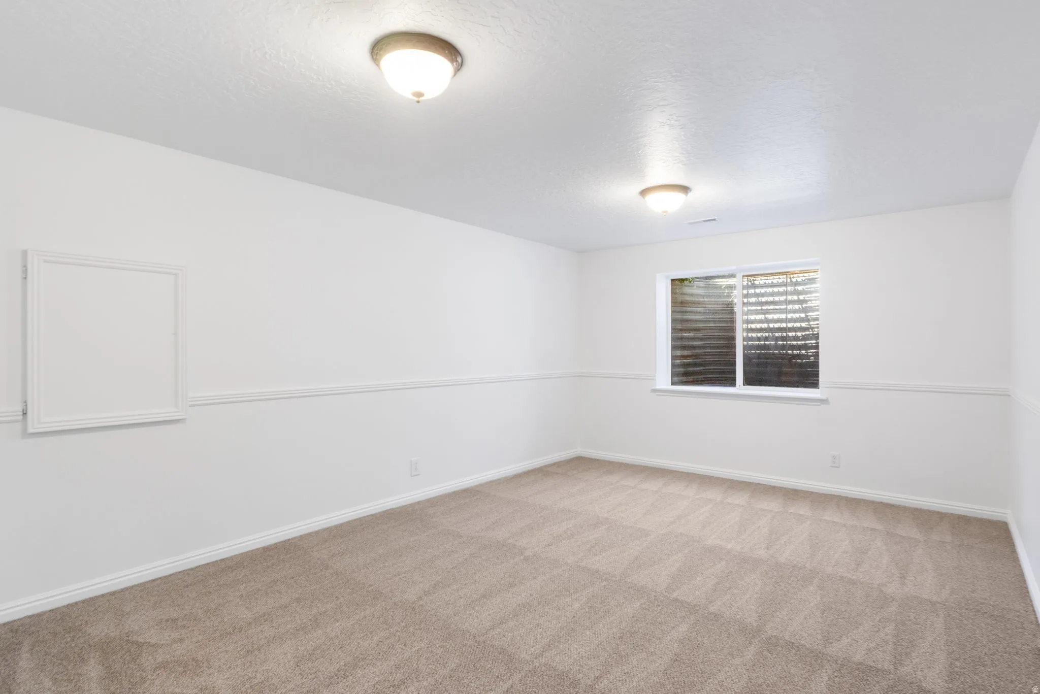 Neutral tone carpeted room featuring white walls, a white window frame, and two flush-mount ceiling lights
