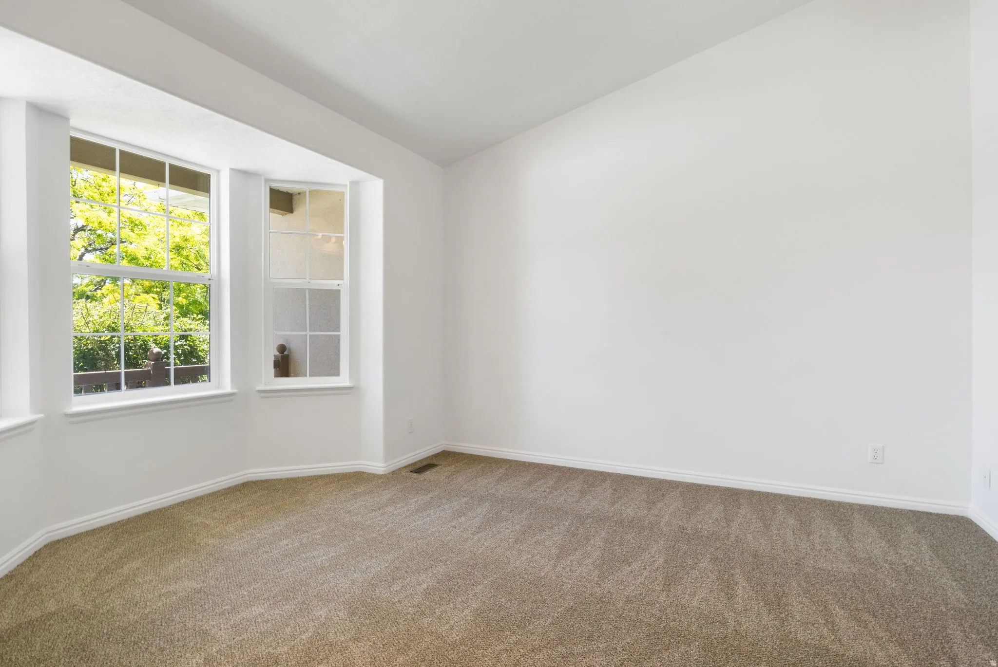 Bright interior space featuring a bay window with multiple panes, vaulted ceiling, and neutral-toned carpet flooring