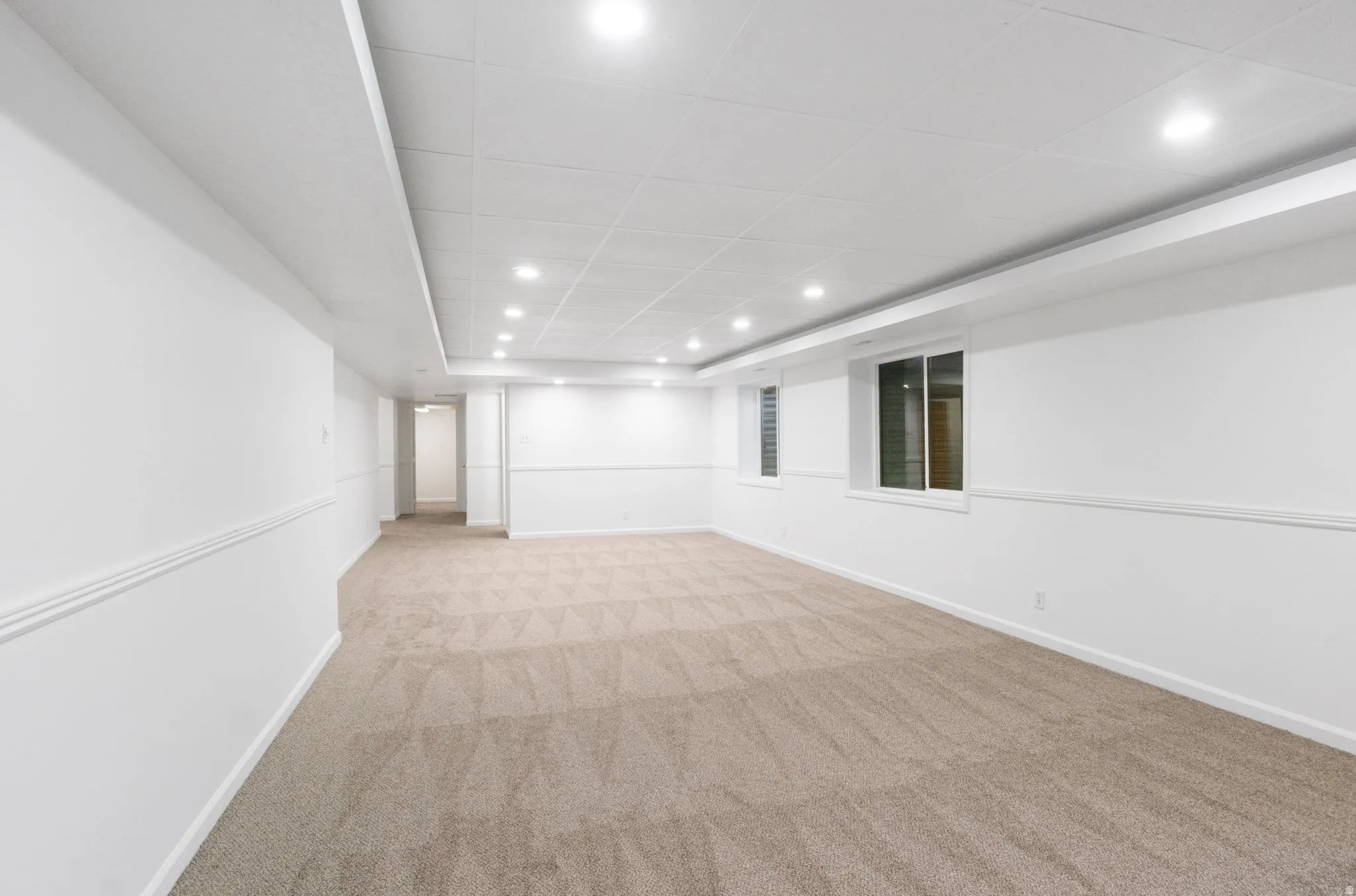 Spacious room featuring neutral carpeting, white walls with chair rail molding, recessed lighting, and two windows