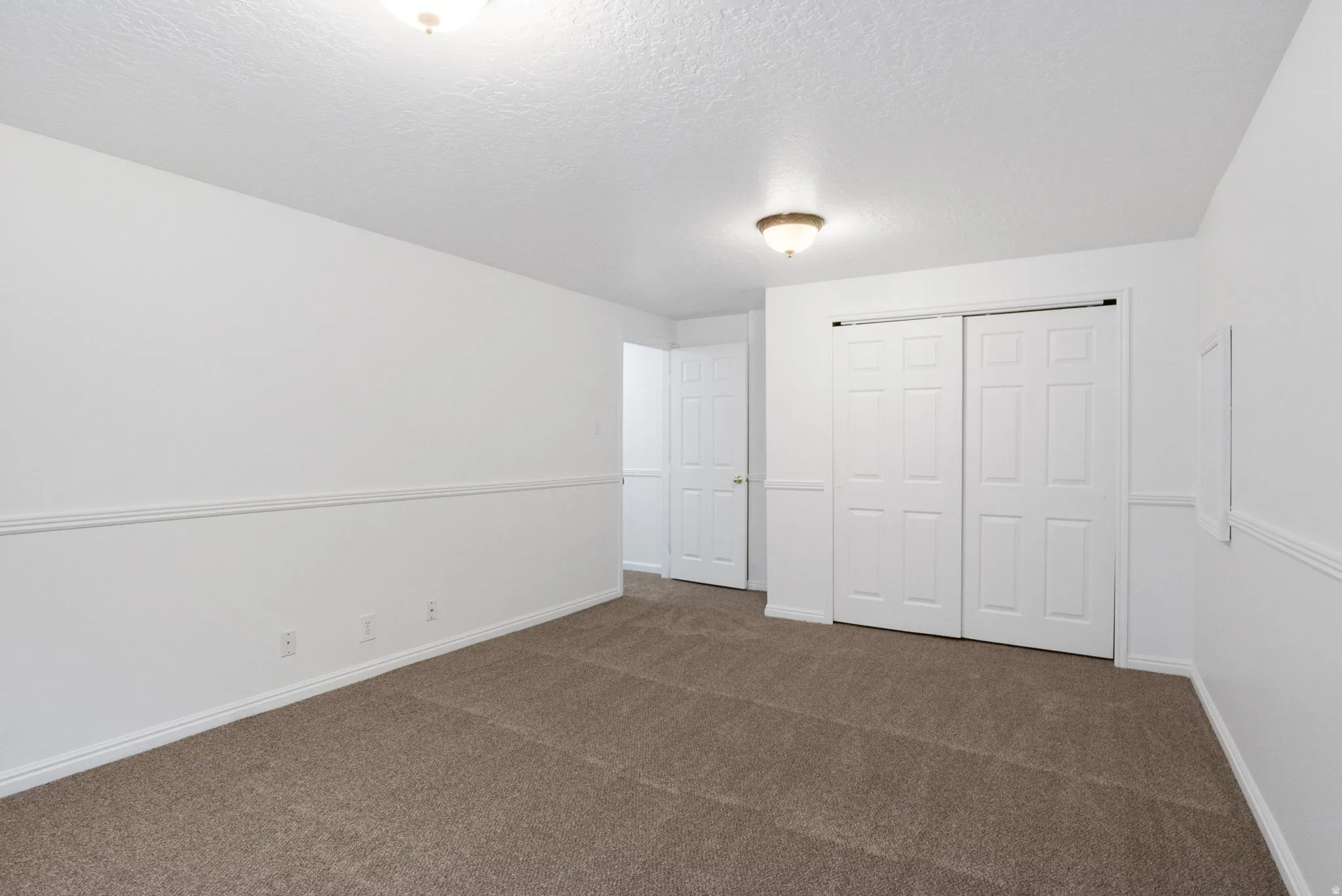 Spacious room featuring neutral carpeting, white walls, and a chair rail molding