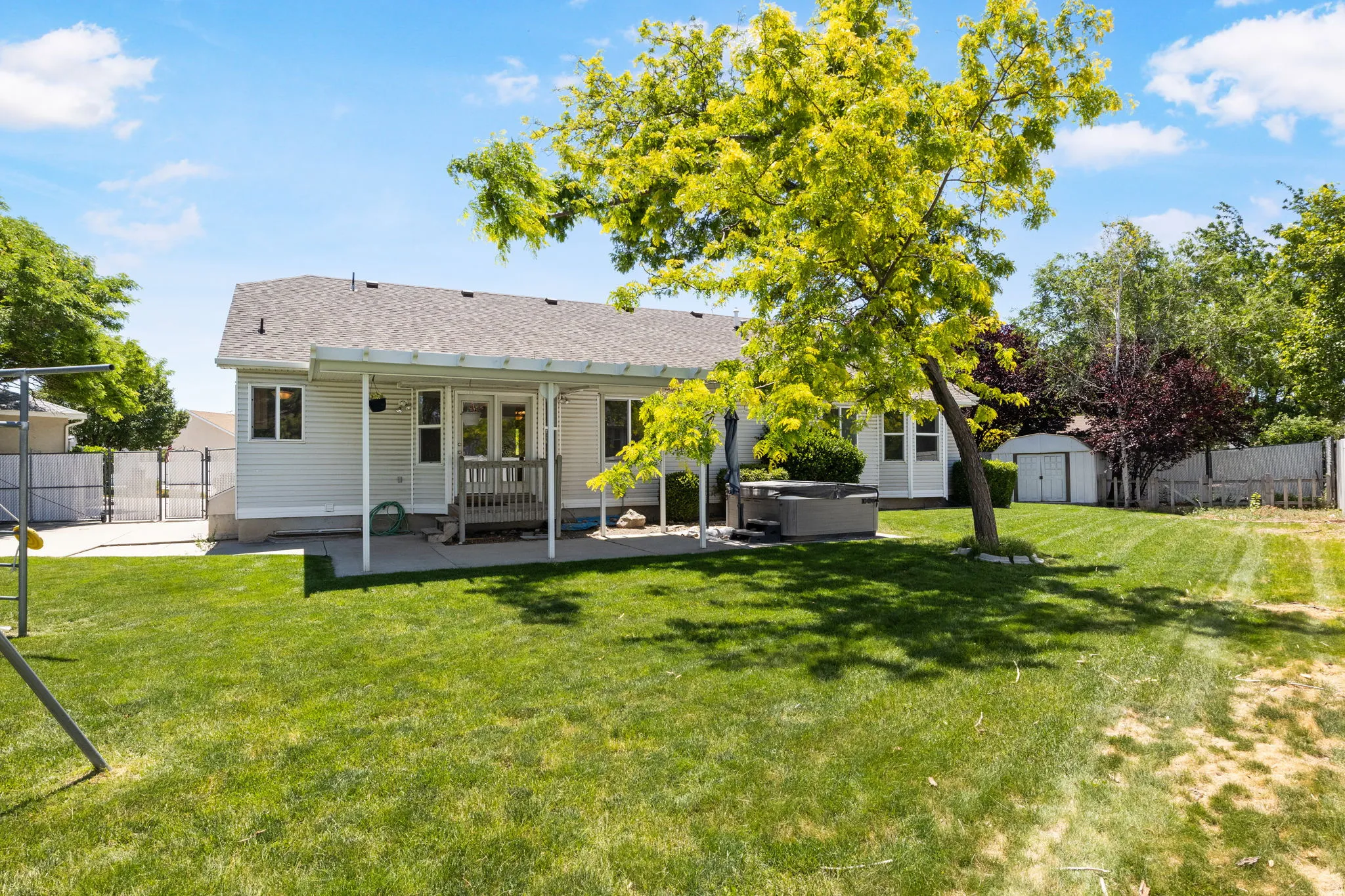 Expansive backyard featuring a manicured lawn, established landscaping, and a covered patio area