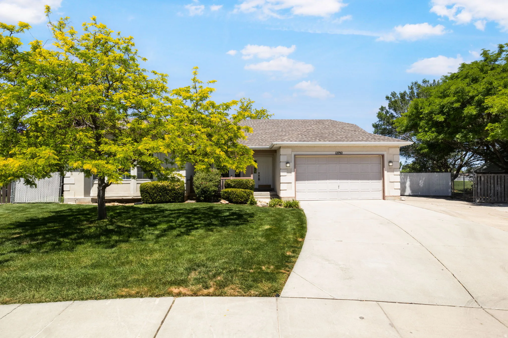 Single-story exterior featuring a two-car garage, concrete driveway, and mature landscaping