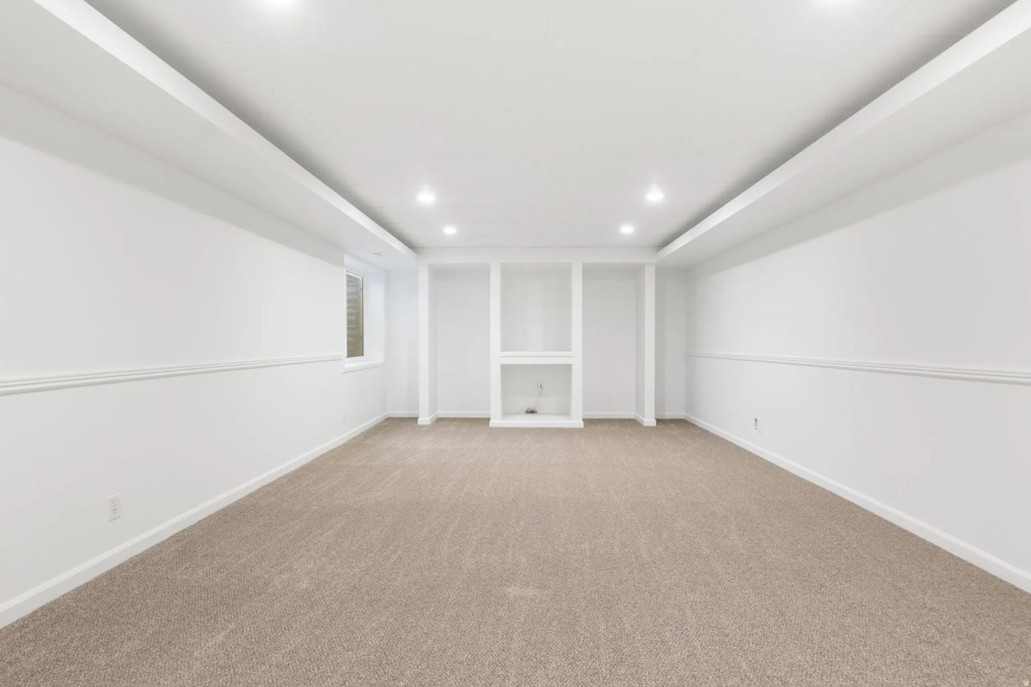 Spacious room featuring neutral carpeting, recessed lighting, and a built-in media center with shelving