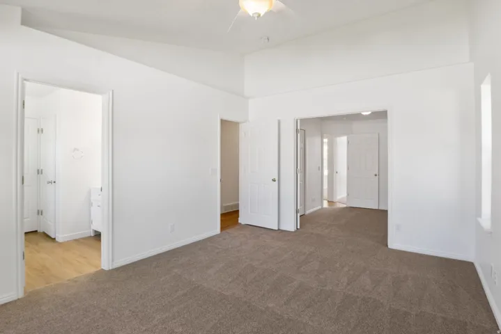 Spacious room featuring vaulted ceilings, neutral-toned carpeting, and multiple doorways