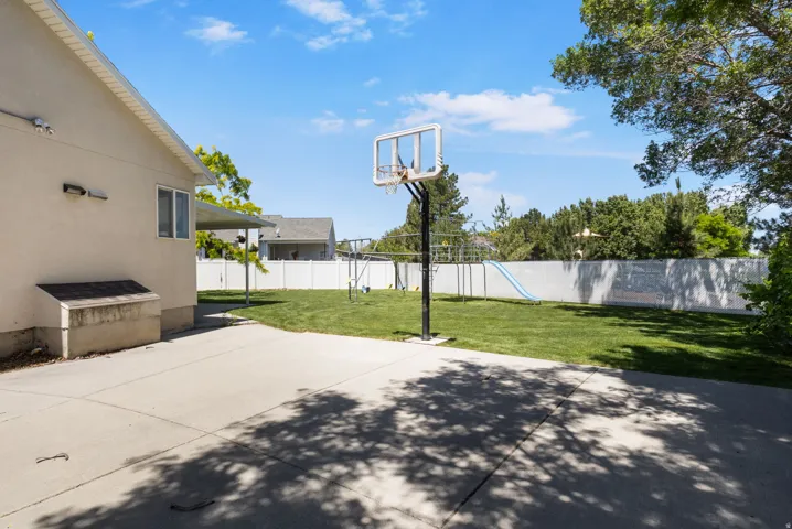 Spacious backyard featuring a concrete patio, a basketball hoop, and a manicured lawn