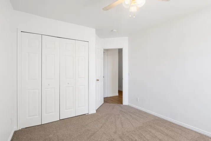 Carpeted room featuring a ceiling fan with light fixture, bifold closet doors, and white baseboards