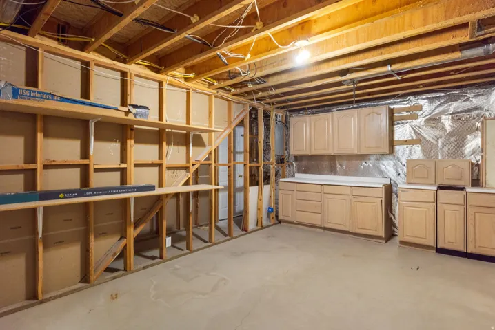 Unfinished basement with exposed wood framing, concrete flooring, built-in shelving, and installed cabinetry with countertops