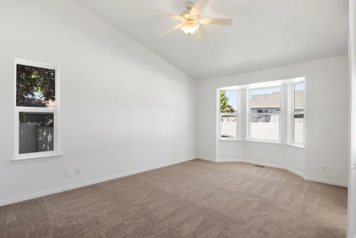 Spacious room featuring a bay window, a single vertical window, sloped ceilings, a ceiling fan with light fixture, and neutral carpet flooring