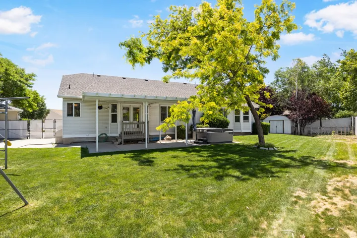 Expansive backyard featuring a manicured lawn, established landscaping, and a covered patio area