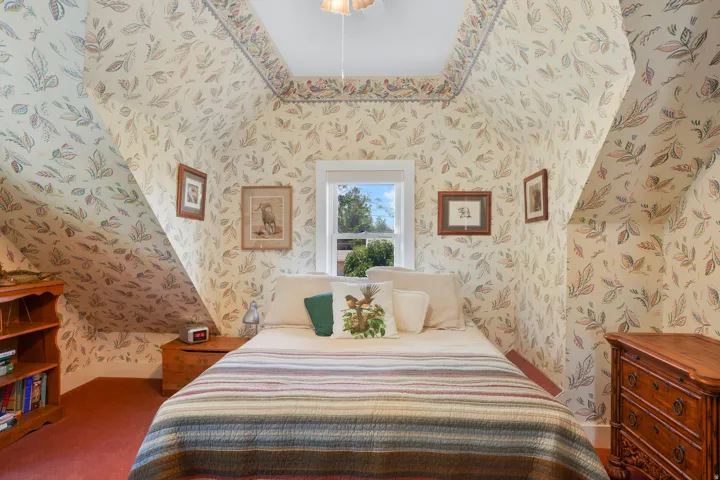 Room featuring sloped ceilings with leaf-patterned wallpaper, a single window, and red carpeting