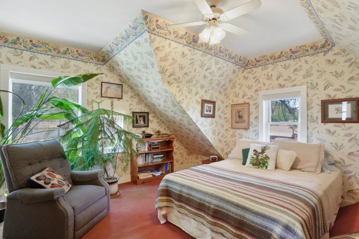 Attic room with sloped ceilings and red carpeting, featuring two windows with white trim, and a ceiling fan with light fixture