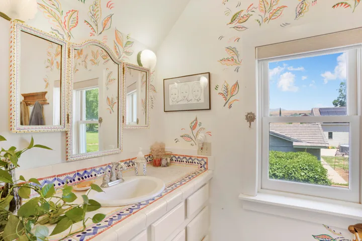 Bathroom featuring a single vanity with a white ceramic sink, tile countertop with decorative trim, and a three-panel mirror