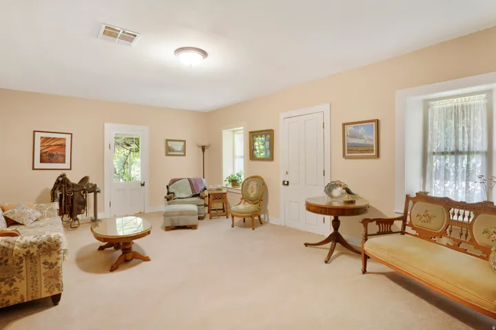 Spacious room featuring neutral carpeting, a light-colored wall palette, multiple windows, and a white paneled door