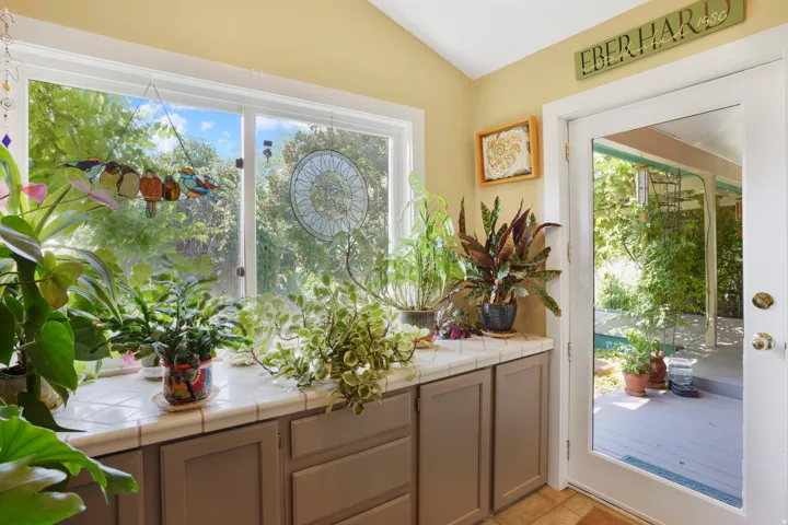 Expansive window above a tiled countertop, featuring under-counter cabinetry and a glass-paneled door leading to an outdoor covered patio area
