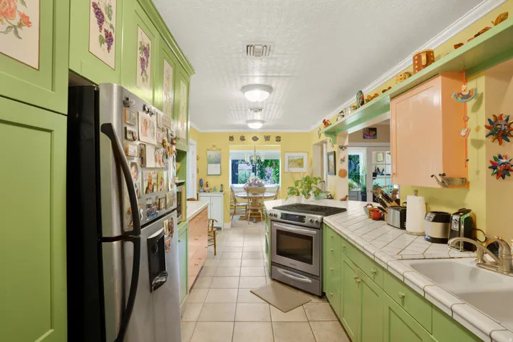 Galley kitchen featuring light green cabinetry, white tile countertops, stainless steel range, and tile flooring