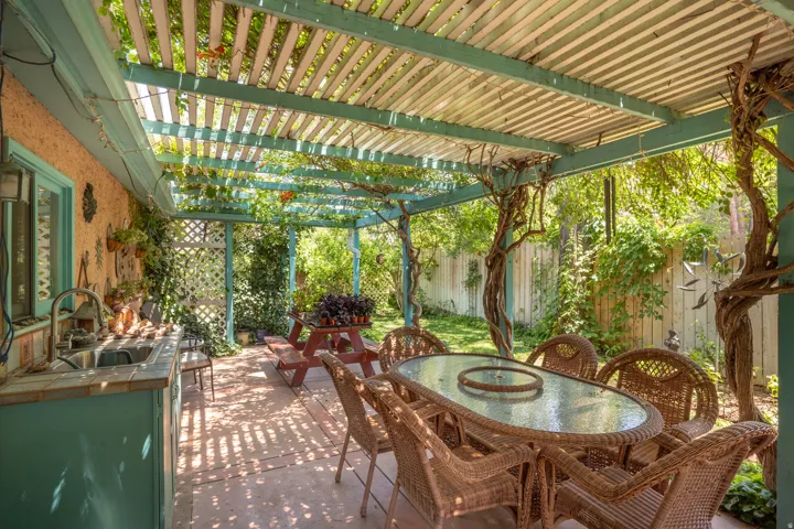 Expansive covered patio featuring a slatted pergola, integrated outdoor sink with tiled countertop, and an adjacent wood-paneled fence