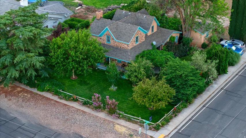 Stone facade residence featuring a multi-gabled roofline, substantial mature landscaping, front lawn, and a light-colored picket fence