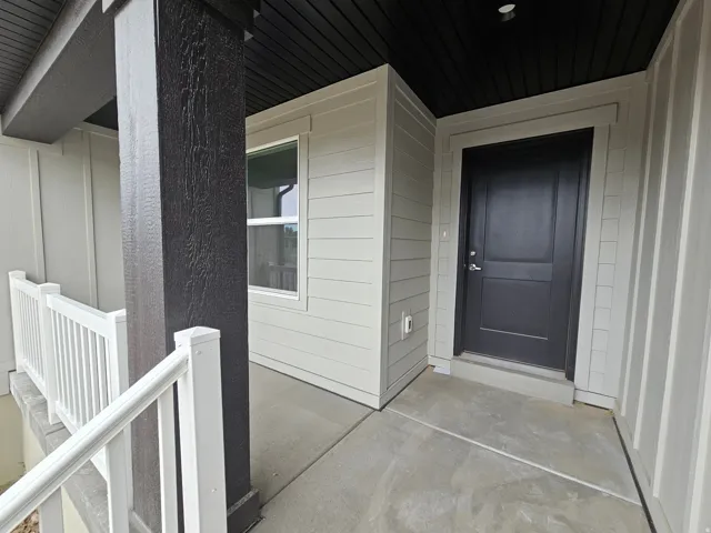 Covered front porch featuring a dark wood-finish support column, white railings, and a dark paneled entry door