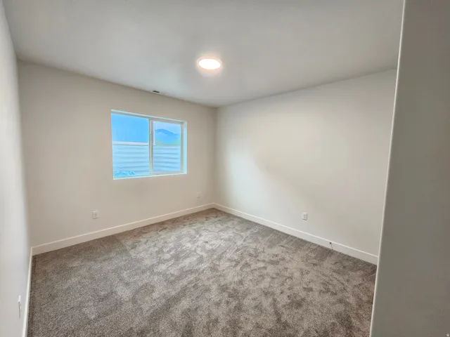 Neutral-toned carpeting, white walls, a single rectangular window, and a ceiling-mounted light fixture