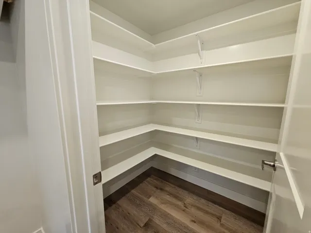 Corner pantry with multiple white built-in shelves and wood-finish flooring