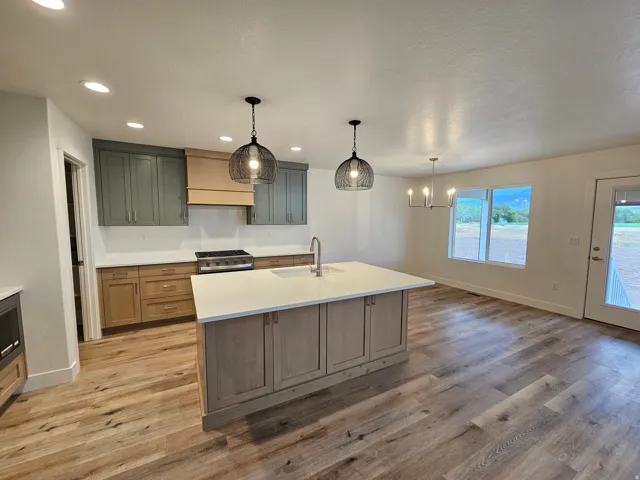 Gourmet kitchen with two-tone cabinetry, a central island featuring a white countertop, stainless steel range, and wood-finish flooring throughout