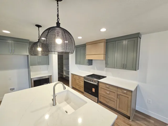 Kitchen featuring a large island with an undermount sink, pendant lighting, stainless steel range, light-toned wood-finish lower cabinetry, and contrasting upper cabinetry