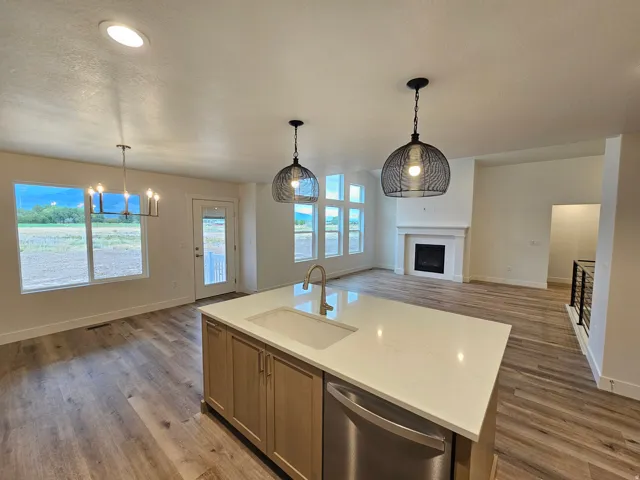 Open-concept living space featuring wood-finish flooring, a kitchen island with integrated sink, stainless steel appliance, and a fireplace with a mantel
