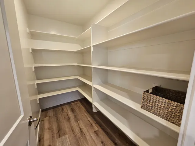 Walk-in pantry featuring extensive built-in shelving, durable wood-finish flooring, and a panel door with a satin nickel handle