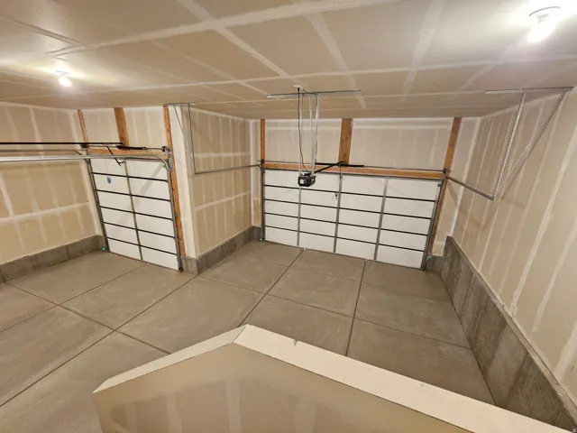 Two-car garage featuring a concrete floor, two garage door openers, and ceiling-mounted lighting