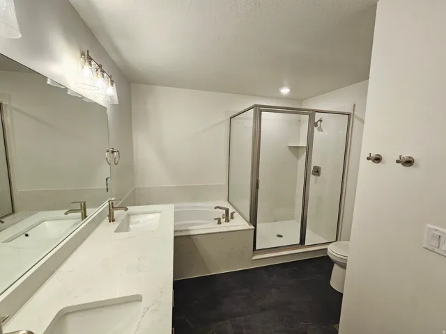 Dual vanity with integrated sinks, a built-in soaking tub, a separate glass-enclosed shower, and dark-toned flooring