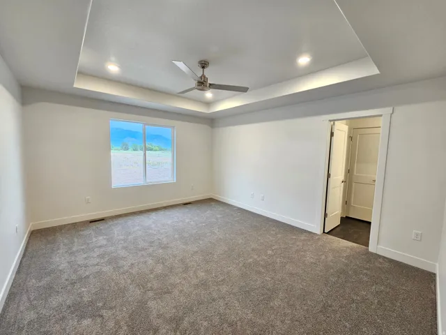 Recessed lighting, tray ceiling, ceiling fan, expansive window, and neutral carpeting