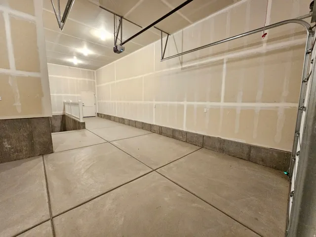 Concrete flooring, drywall walls, overhead lighting, door access, and a built-in railing