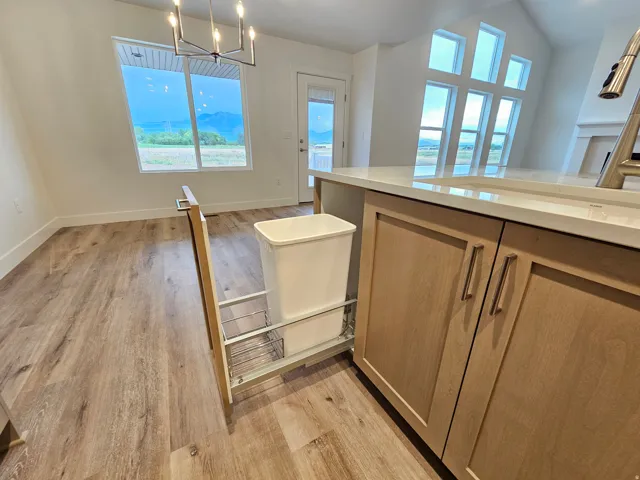 Wood-finish flooring, contemporary chandelier, kitchen island with light-toned cabinetry and integrated pull-out waste bin, light-toned countertop, and expansive window with mountain backdrop