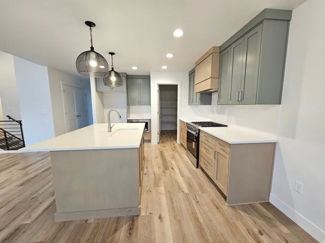 Kitchen featuring an expansive island with a stainless steel sink, wood-finish flooring, two-tone cabinetry, stainless steel range, and recessed lighting