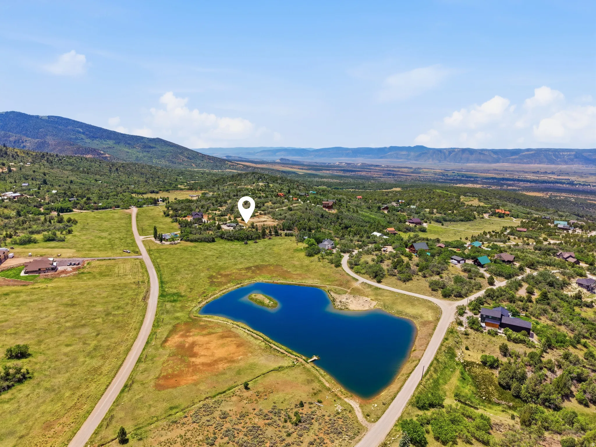 Expansive property featuring a private pond with a central island, surrounded by a natural landscape of mature trees and open fields