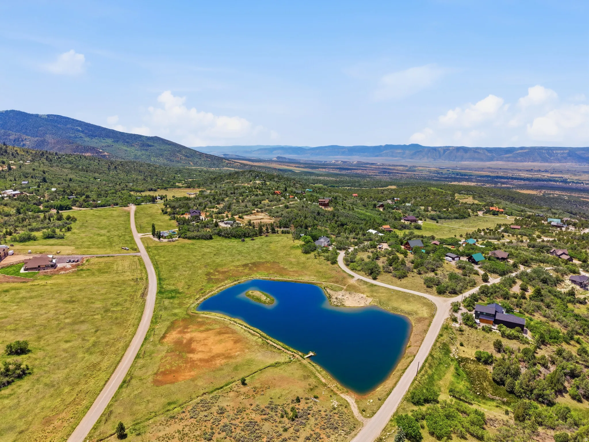 Expansive aerial landscape featuring a private pond with a small island, surrounded by scattered residential properties