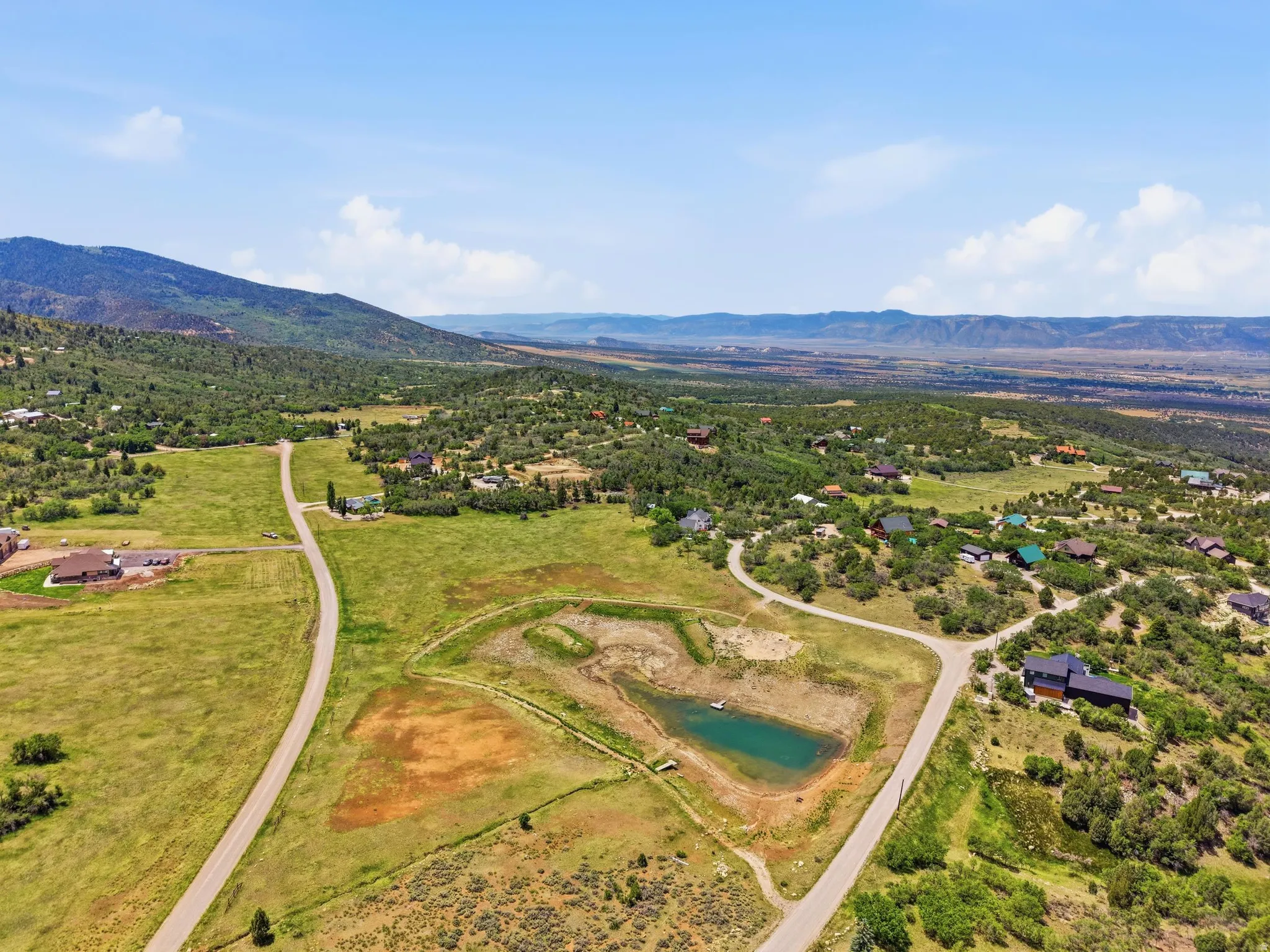 Expansive rural landscape featuring a private pond, paved roads, scattered residences, and distant mountain ranges
