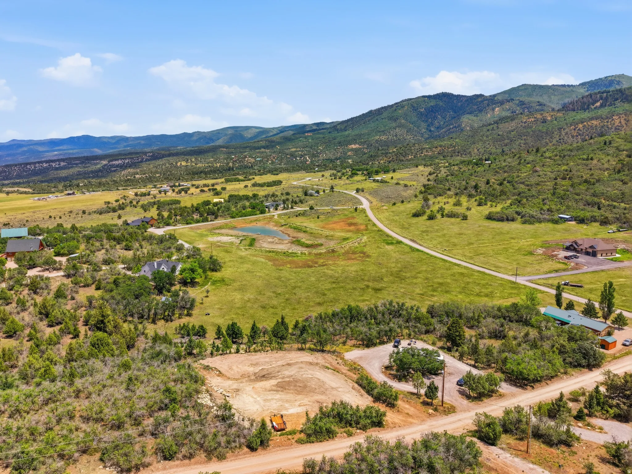 Expansive rural landscape featuring a private road, multiple parcels, green fields, and distant mountains under a blue sky