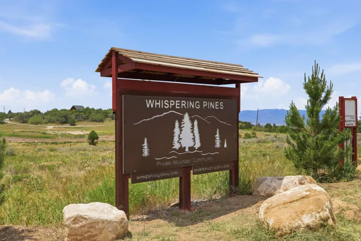 Entry sign for a private mountain community, featuring a brown sign with white text and tree graphics, set within a natural, expansive landscape