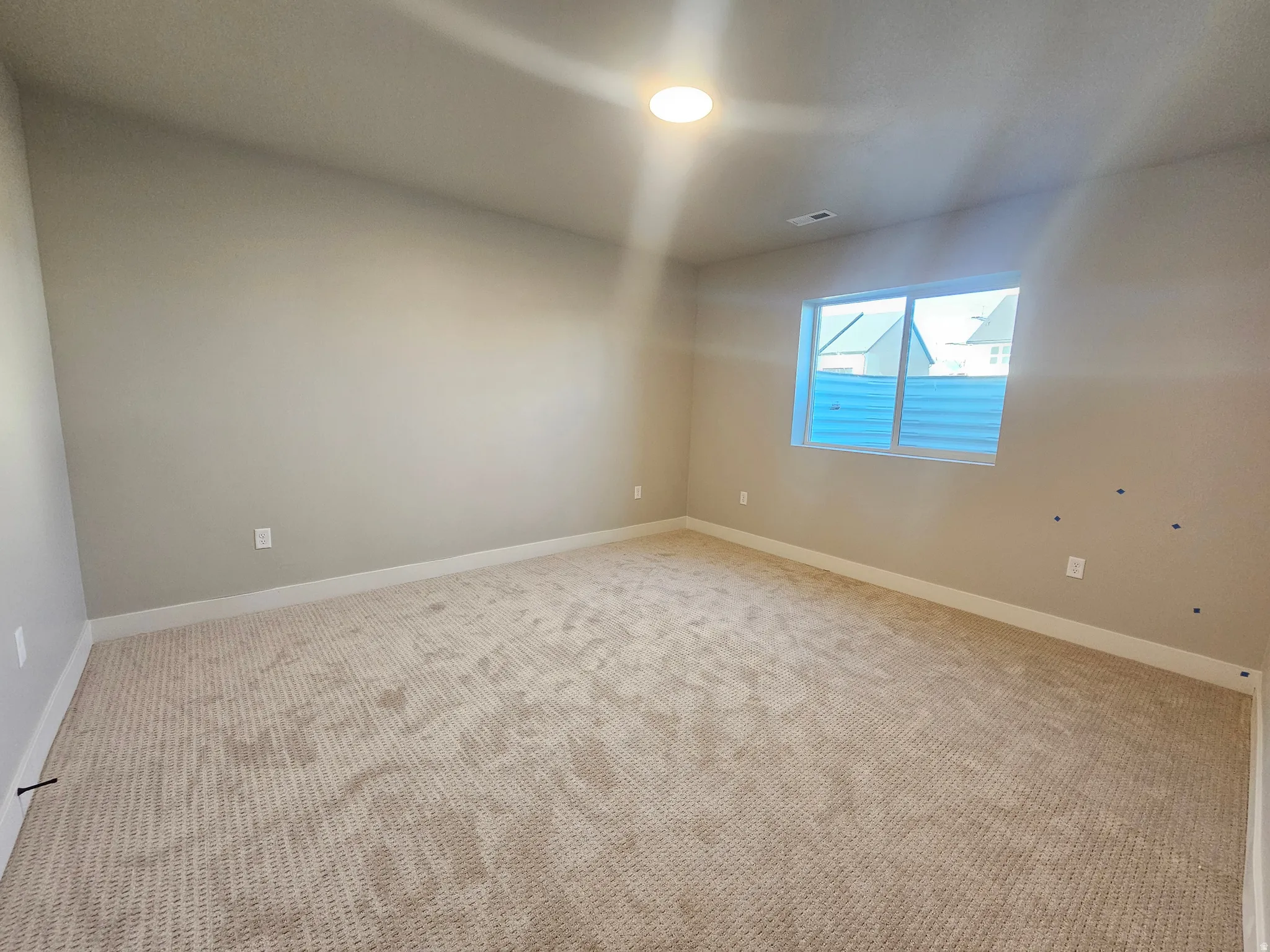 Spacious interior room featuring neutral wall paint, light-colored carpeting, a single window with horizontal blinds, and a ceiling-mounted light fixture