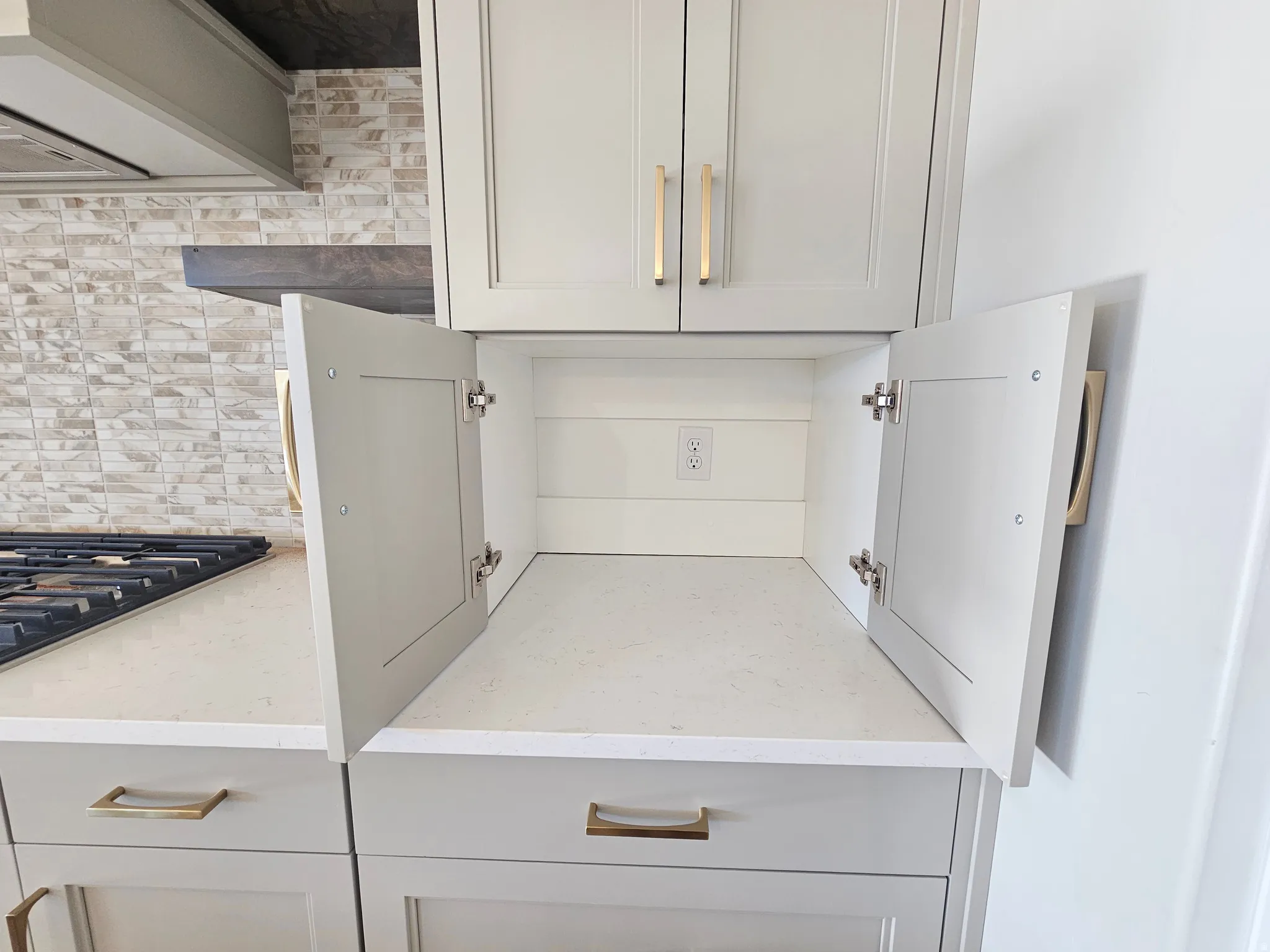 Light gray shaker-style cabinetry with gold-finish hardware, quartz countertops, and a subway tile backsplash