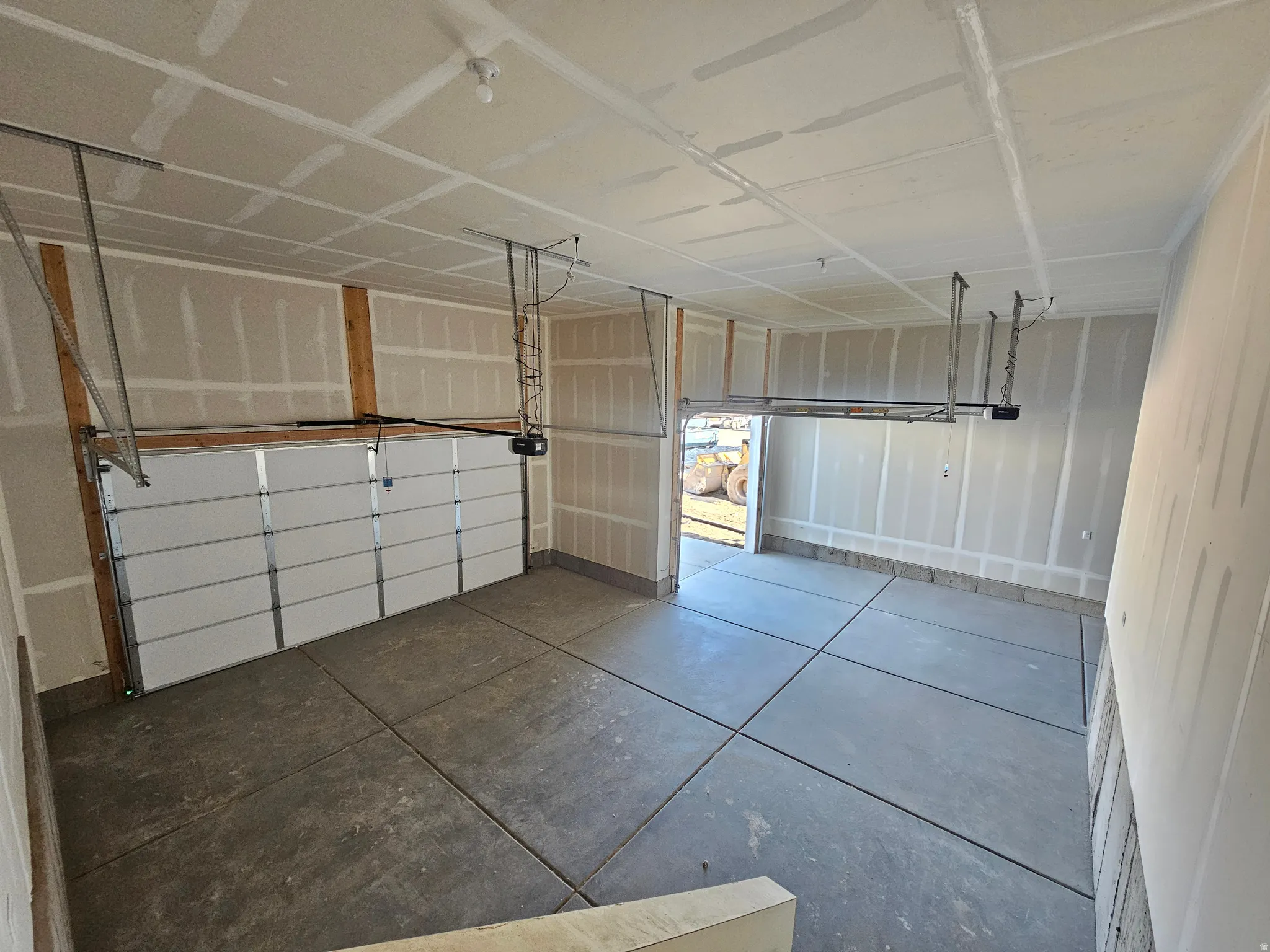 Spacious two-car garage featuring segmented overhead doors with openers, a concrete floor, and unfinished drywall walls and ceiling