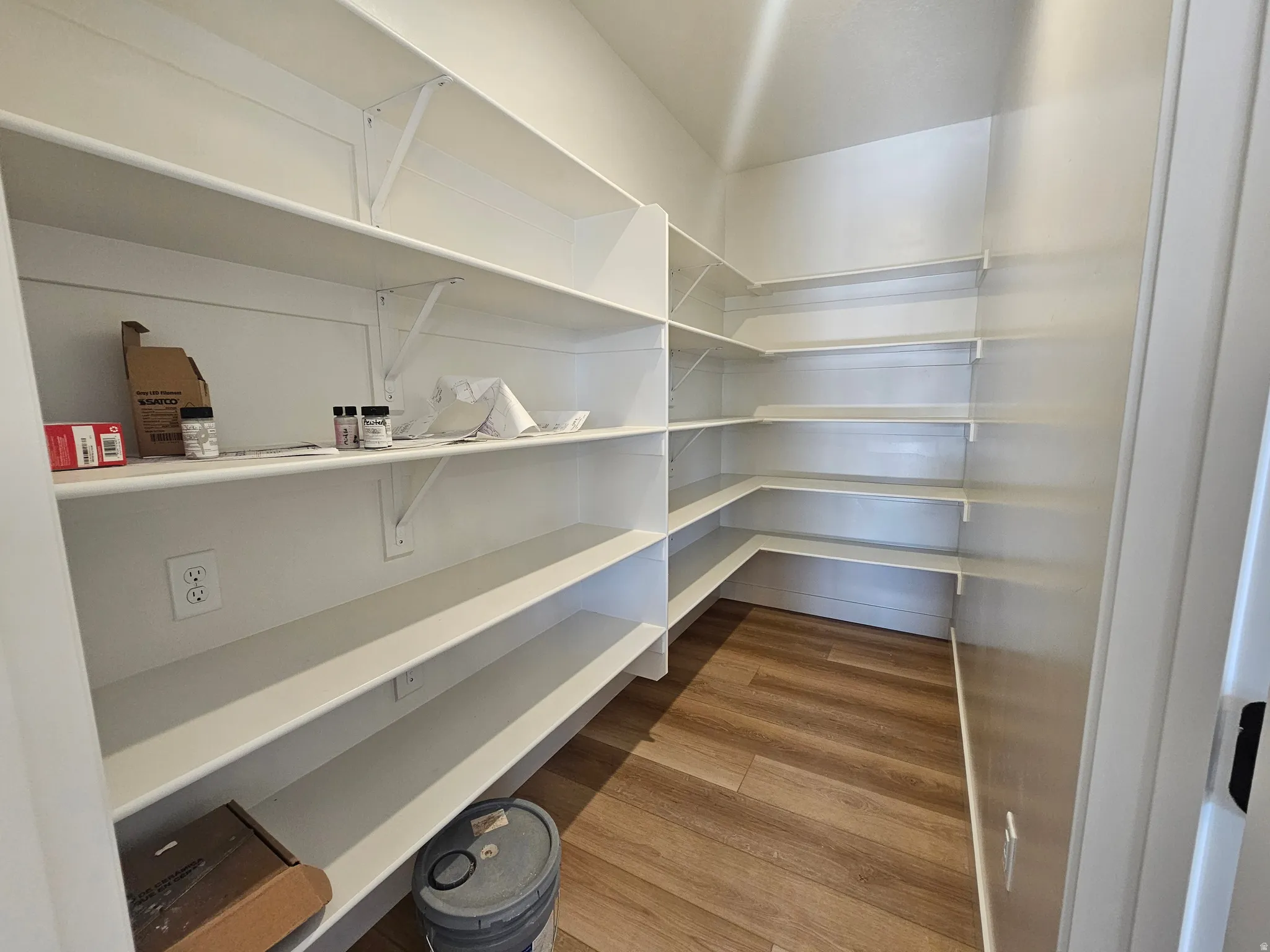 Pantry featuring extensive white shelving, corner shelf configurations, and wood-finish flooring