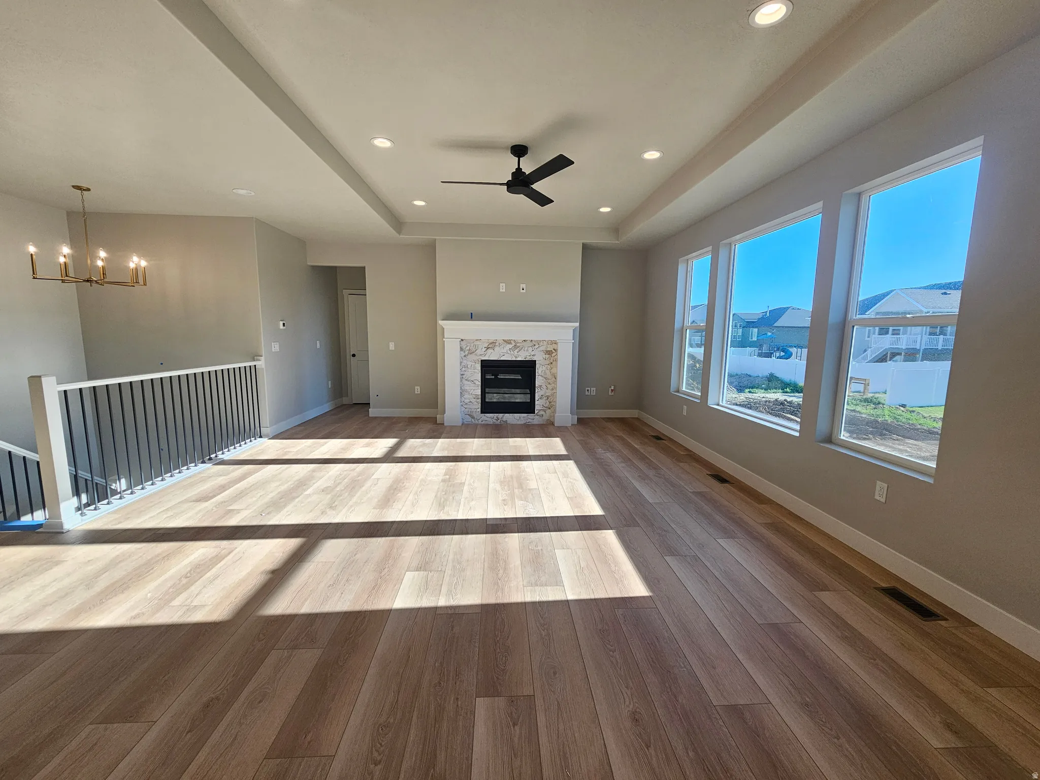 Open-concept living space featuring wood-finish flooring, a contemporary fireplace with a stone surround and mantel, and multiple large windows