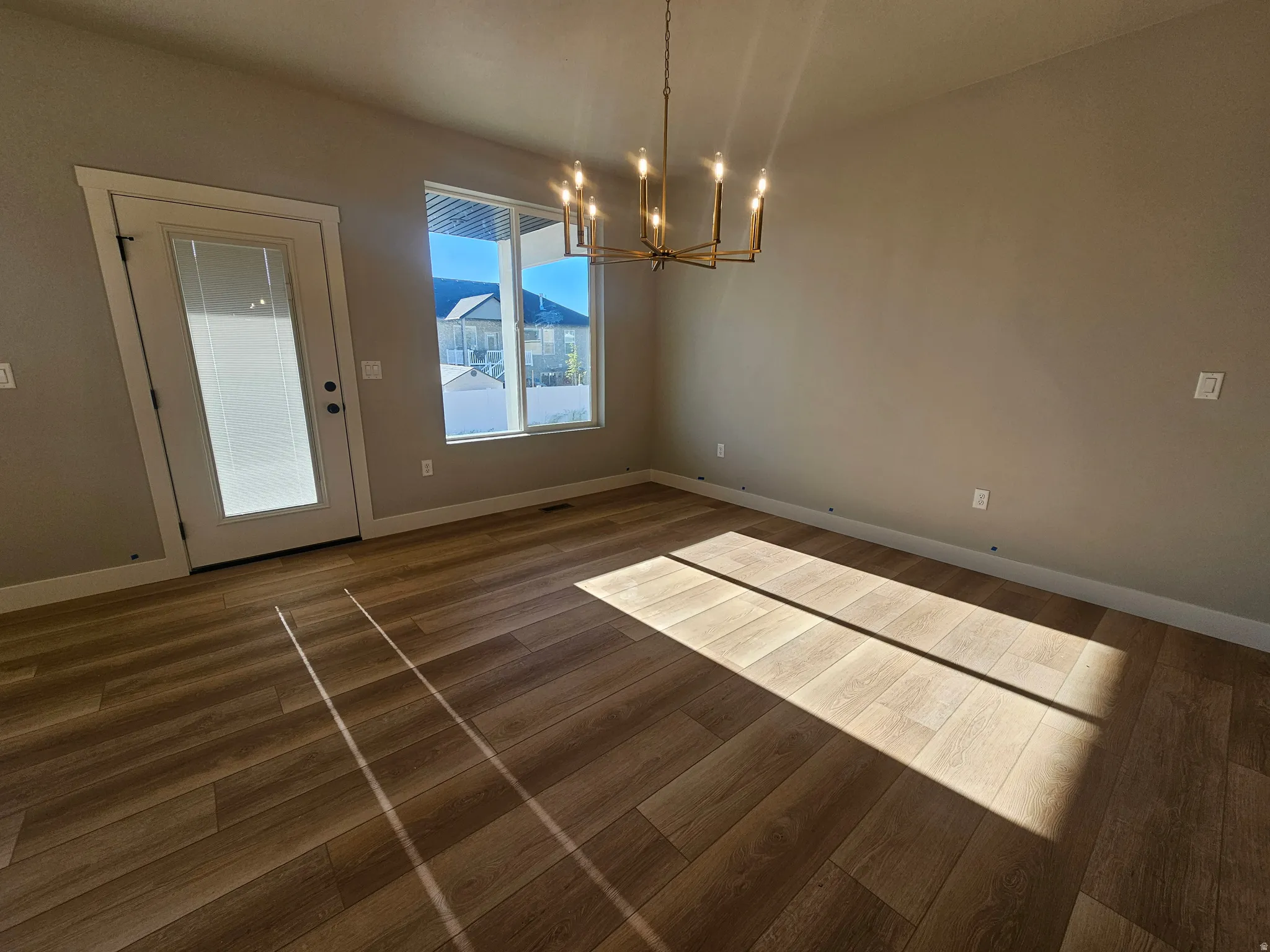 Spacious room featuring wood-finish flooring, a contemporary brass chandelier, and neutral wall tones