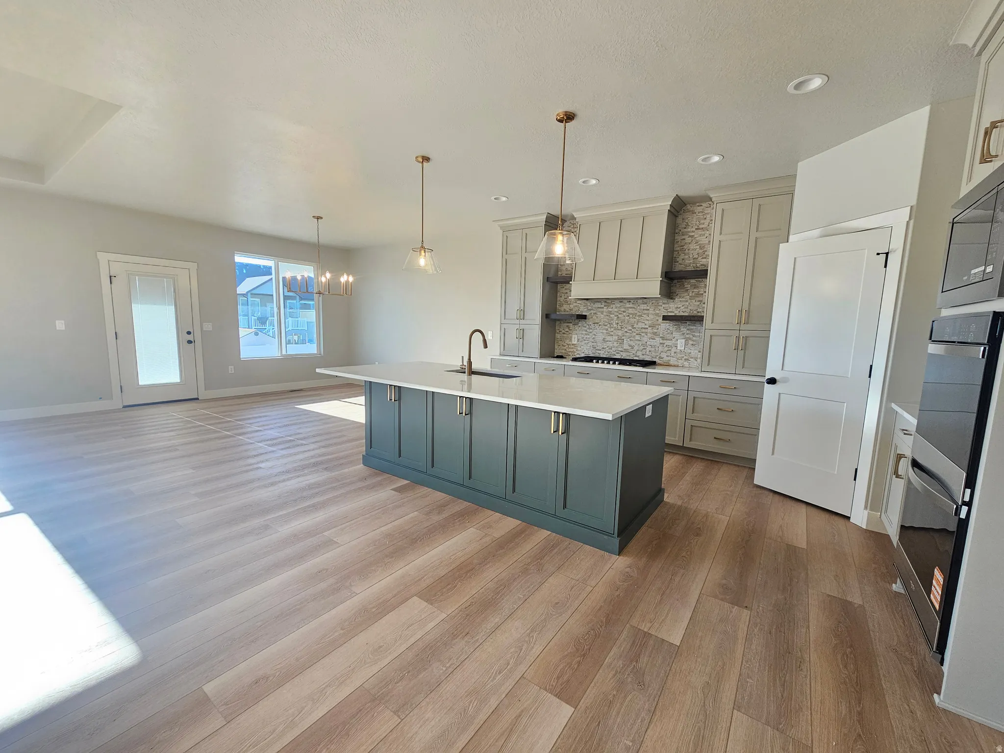 Open-concept kitchen featuring an island with a contrasting finish, pendant lighting, built-in stainless steel appliances, and wood-finish flooring